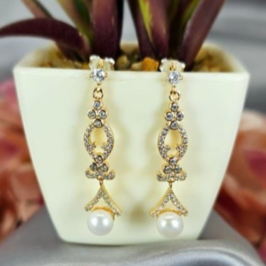 Rose gold long drop earrings with freshwater pearls on end, displayed in a white vase with a green plant in the background.