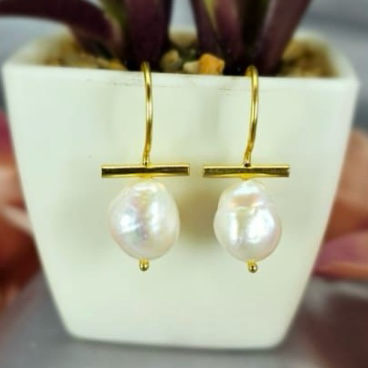 A pair of gold earrings with freshwater pearls on ends, displayed in a white vase with a green plant.