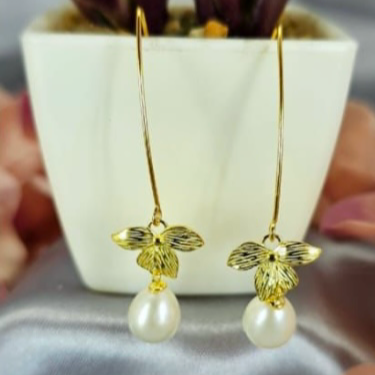 A pair of gold long drop flower-shaped earrings with freshwater pearls on the ends, displayed on a flat surface.