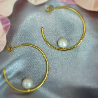 Gold plated sterling silver hoop earrings with freshwater pearls on a silky grey background with flower petals scattered around.