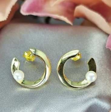 A pair of gold-plated sterling silver C-shaped earrings with freshwater pearls on a textured surface.