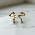 A pair of gold-plated modern wave-shaped earrings with freshwater pearl accents, displayed in a white pot.