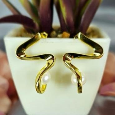 A pair of gold-plated modern wave-shaped earrings with freshwater pearl accents, displayed in a white pot.
