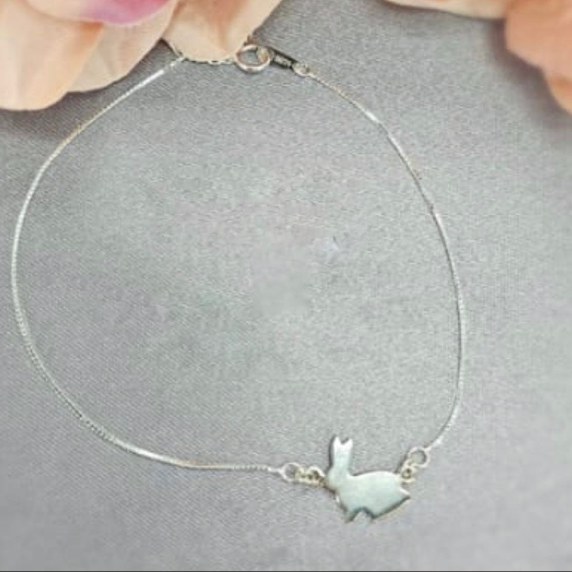 Silver bracelet with a small fish charm held by a hand on a gray background