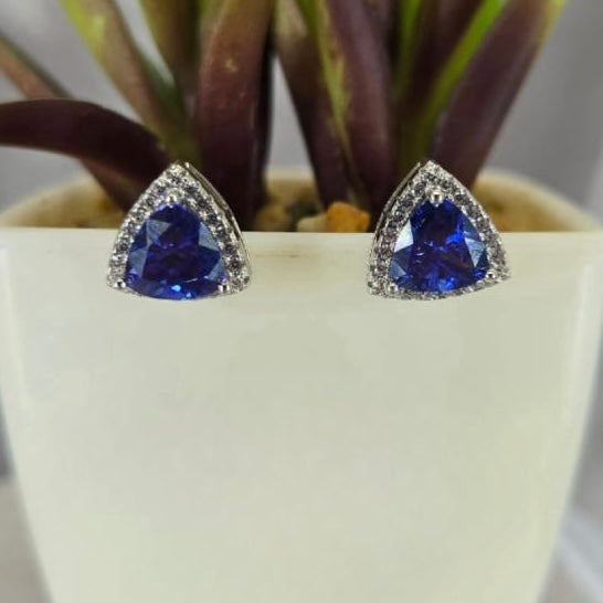 A pair of blue triangle cubic zirconia stud earrings set in sterling silver, displayed against a white plant pot background.