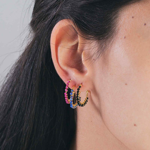 Close-up of an ear wearing colorful hoop earrings with a neutral background