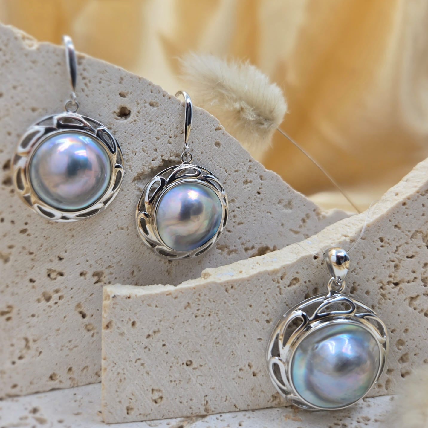 Pearl earrings and pendant on a stone surface with a soft background