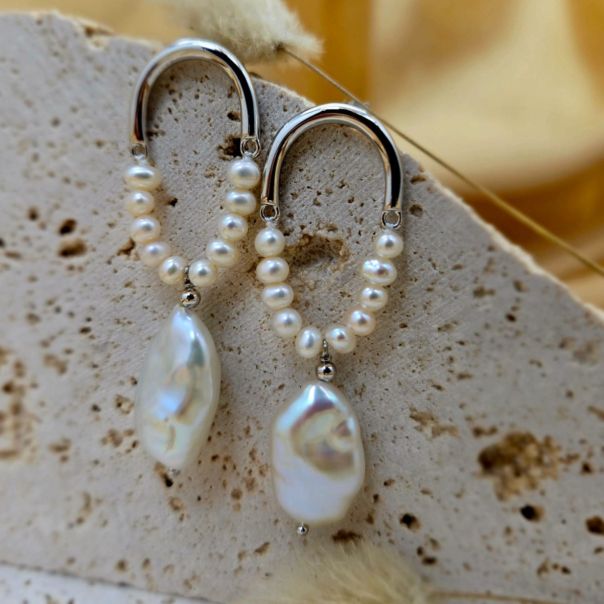 Pearl earrings with silver hooks on a textured surface with a blurred background