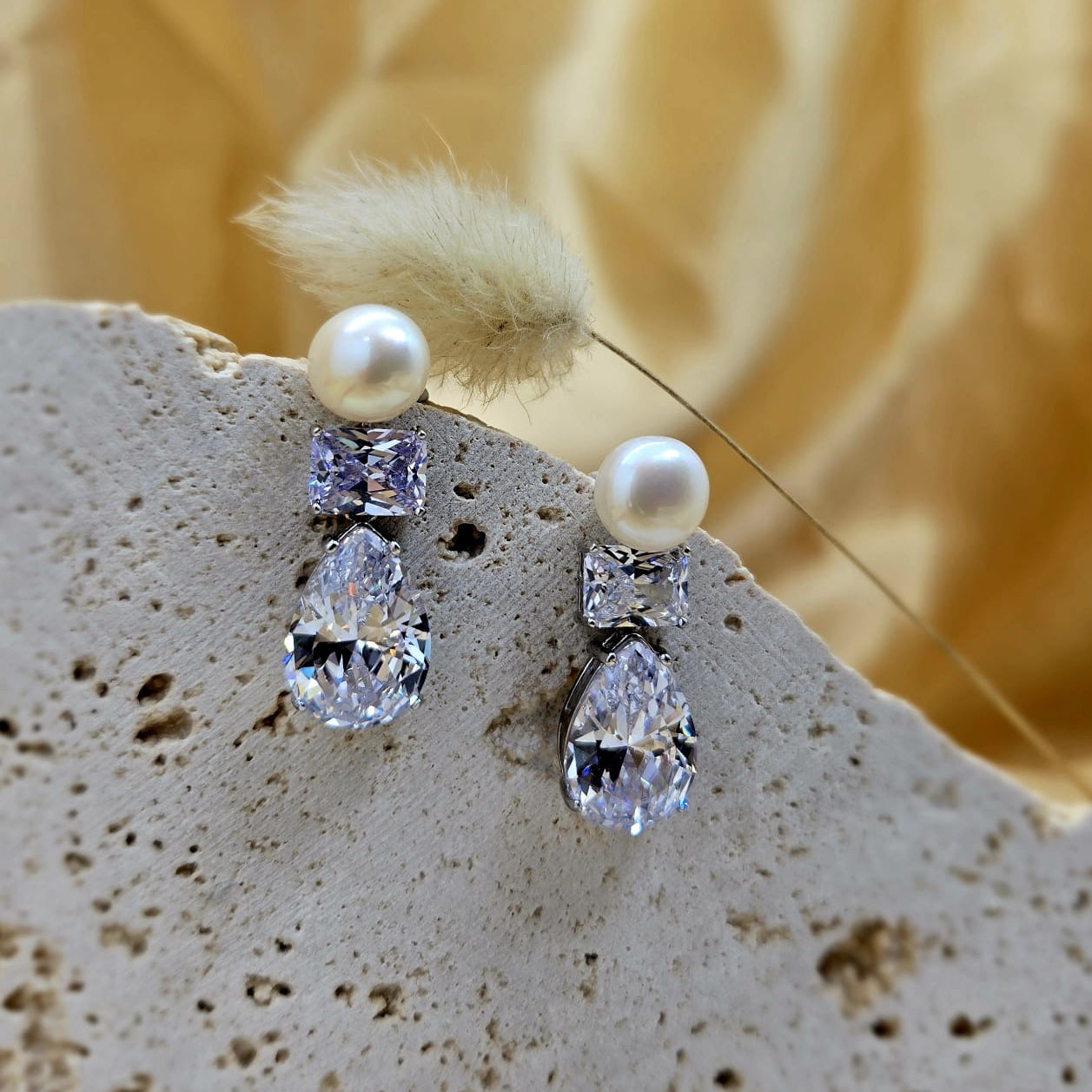 Pearl and crystal earrings on a textured surface with a blurred natural background