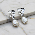 Pair of silver earrings with pearl drops on a textured surface.