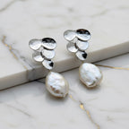Pair of silver earrings with pearl drops on a textured surface.
