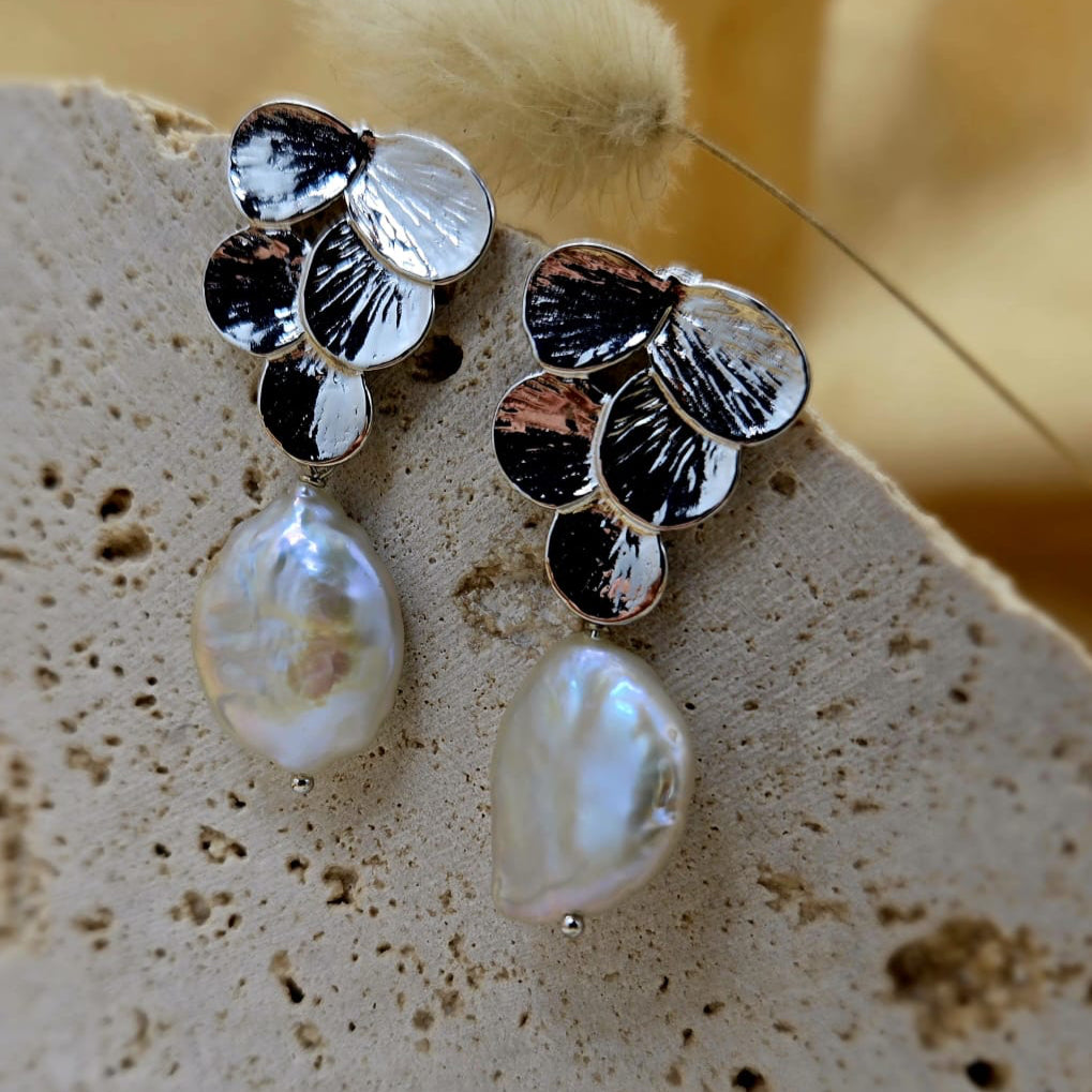 Pair of silver earrings with pearl drops on a textured surface.
