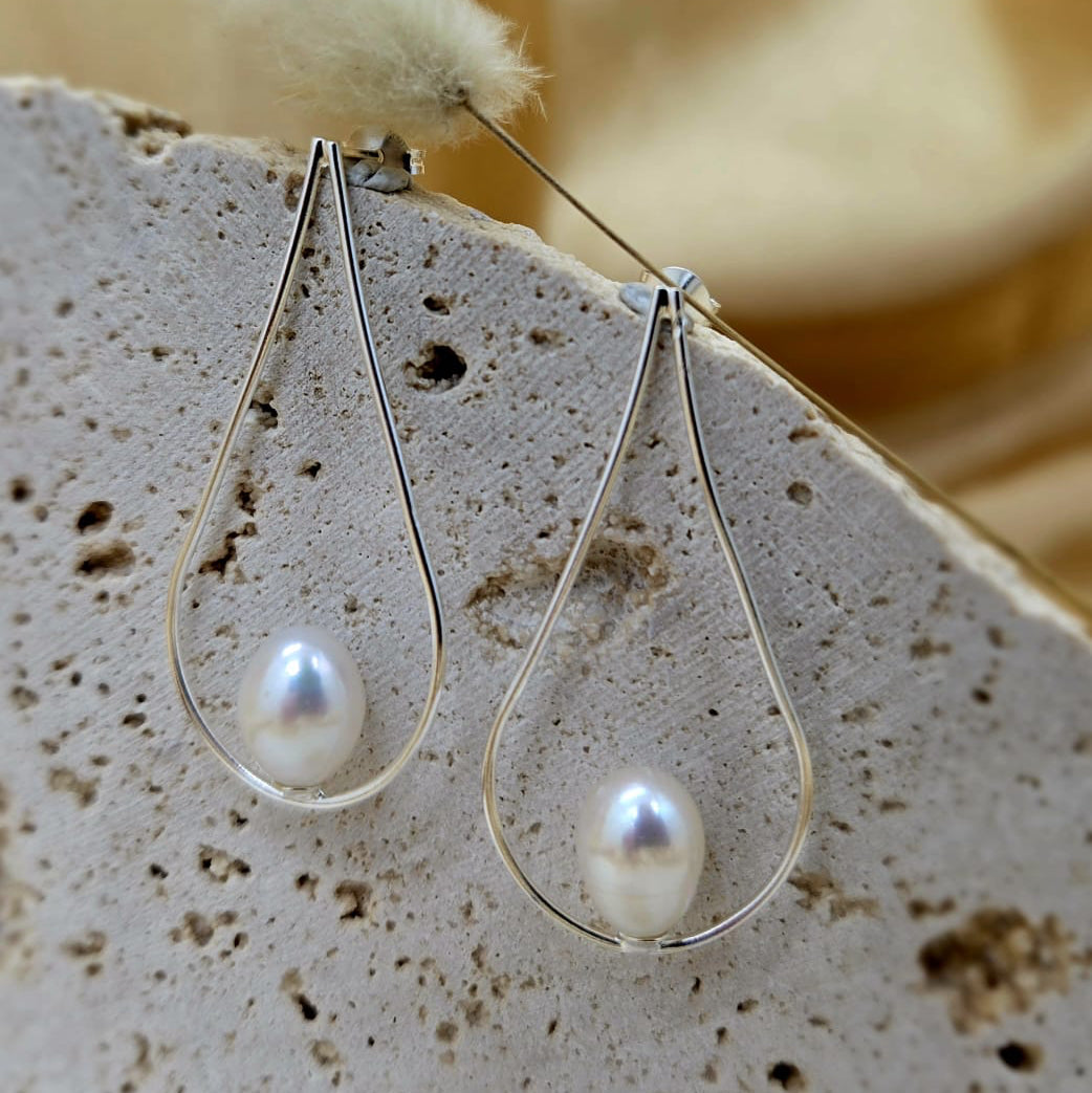 Pearl earrings on a textured stone surface with a soft yellow background
