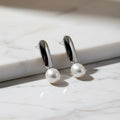 Pearl earrings with gold accents on a textured surface with a blurred yellow background