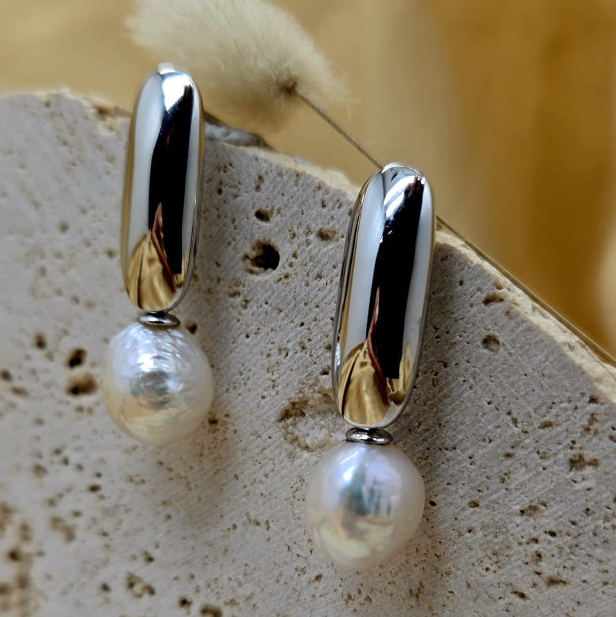 Pearl earrings with gold accents on a textured surface with a blurred yellow background