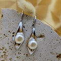 Pearl earrings on a textured stone surface with a blurred yellow background