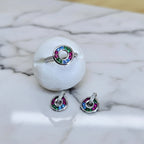 Silver ring with colorful gemstones on a white stone surface with a yellow fabric background