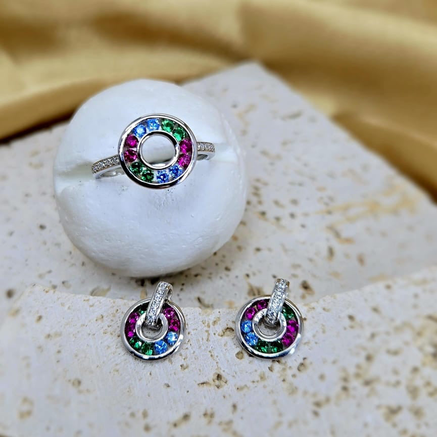Silver ring with colorful gemstones on a white stone surface with a yellow fabric background