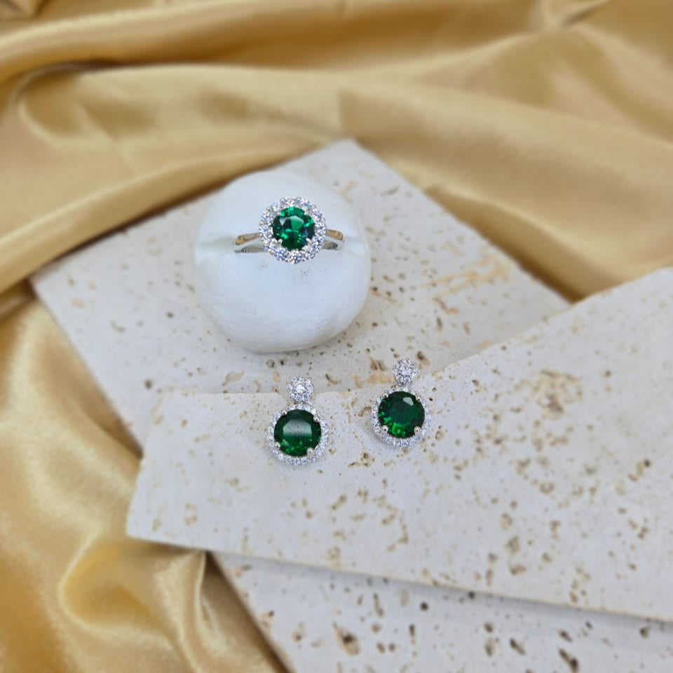 Green gemstone jewelry set on a textured surface with a yellow fabric background