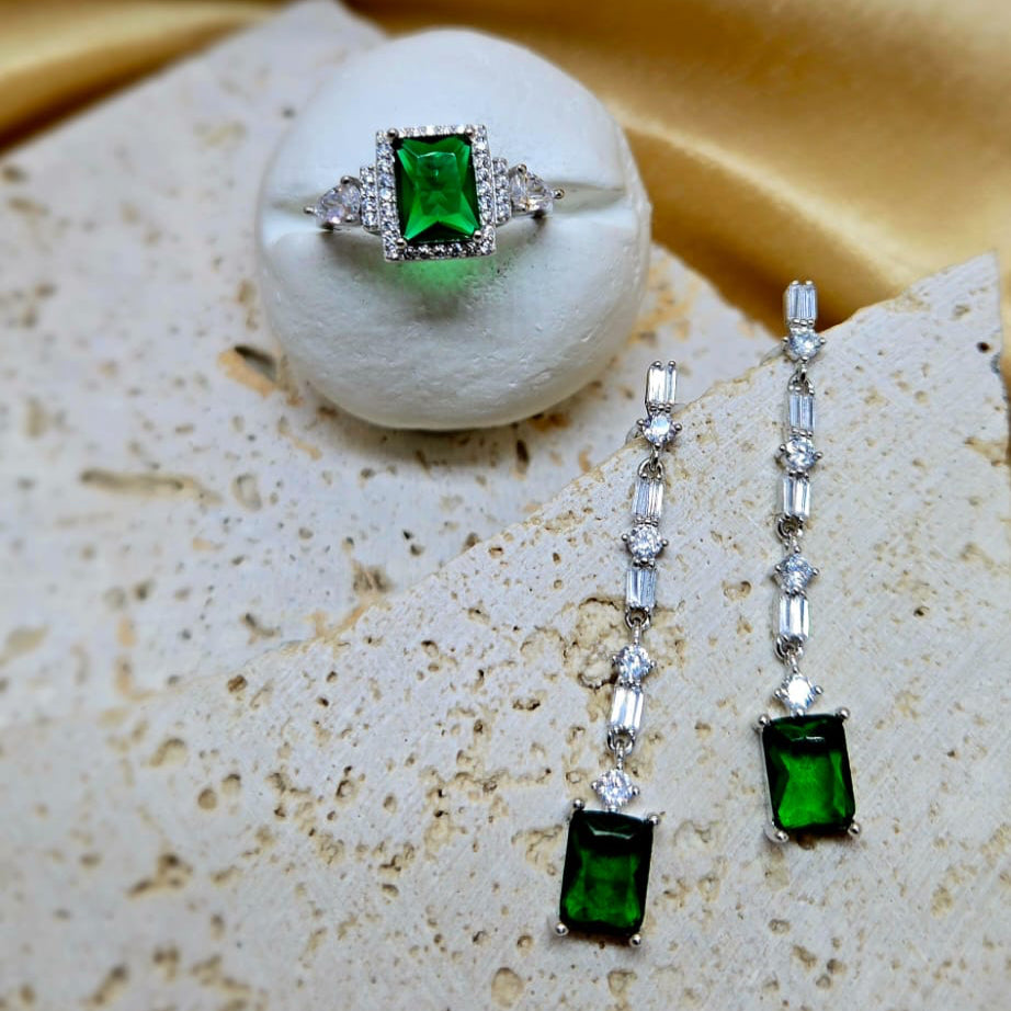 Green gemstone ring and earrings on a textured surface with a yellow fabric background