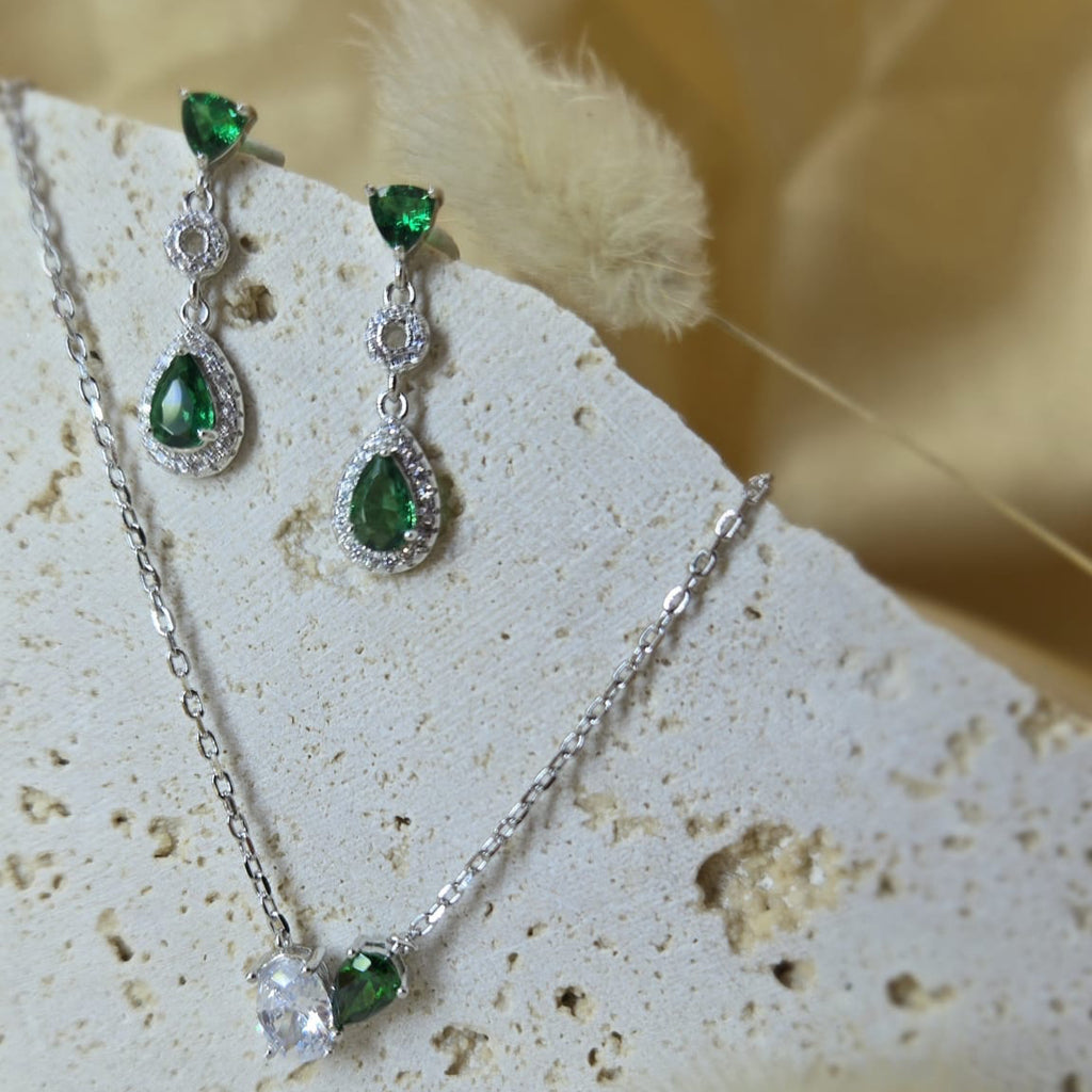 Silver necklace and earrings with green gemstones on a textured surface