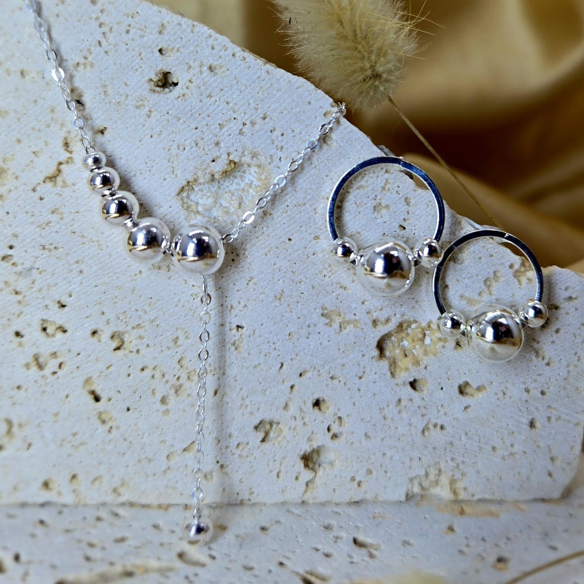 Silver necklace and earrings on a textured surface with a blurred background
