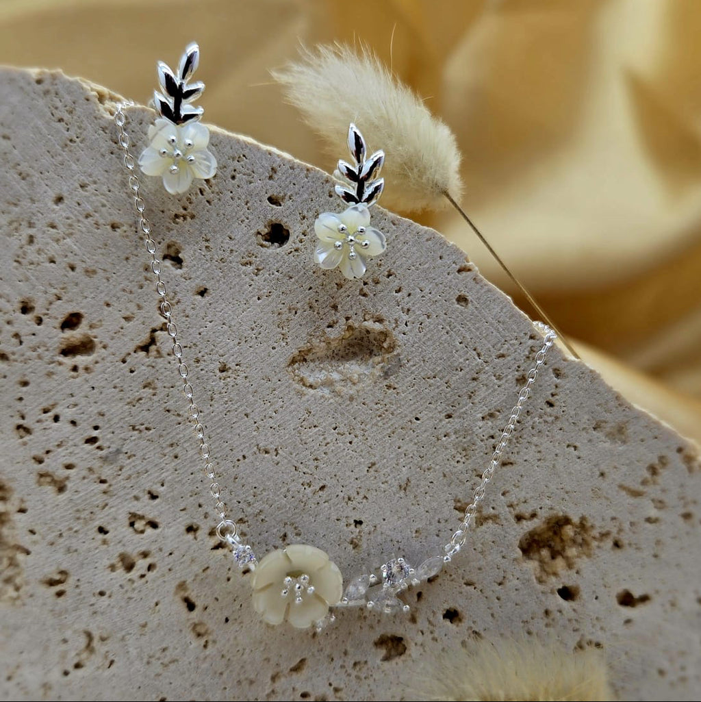 Delicate silver necklace with floral pendants on a textured stone surface
