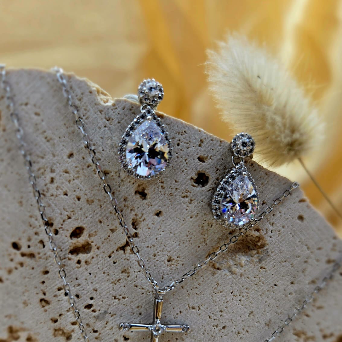 Silver necklace with teardrop-shaped pendants and a cross pendant on a textured surface.