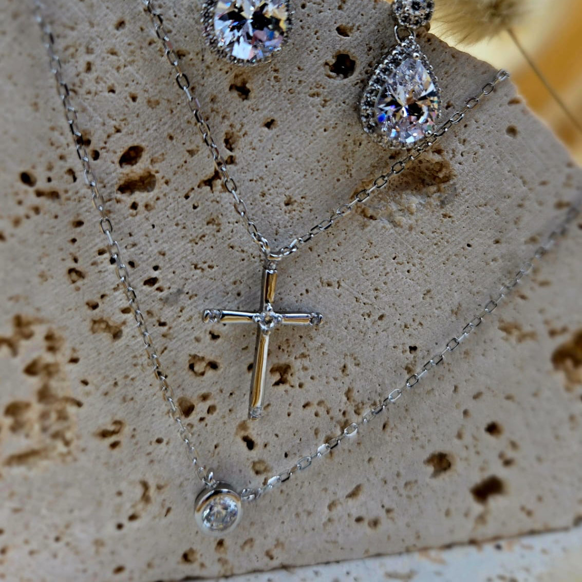 Silver necklace with teardrop-shaped pendants and a cross pendant on a textured surface.