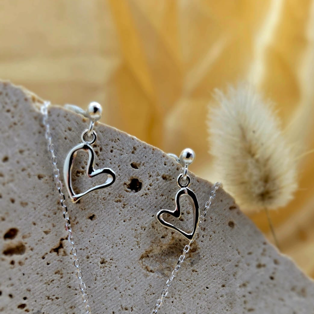 Silver heart-shaped earrings on a stone surface with a blurred natural background