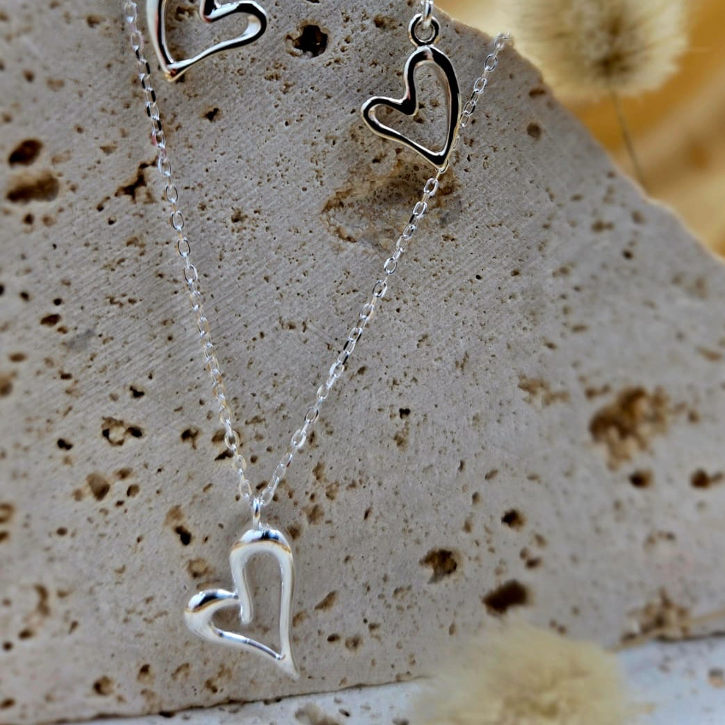 Silver heart-shaped earrings on a stone surface with a blurred natural background