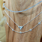 Two silver necklaces with bee and flower charms on a wooden surface