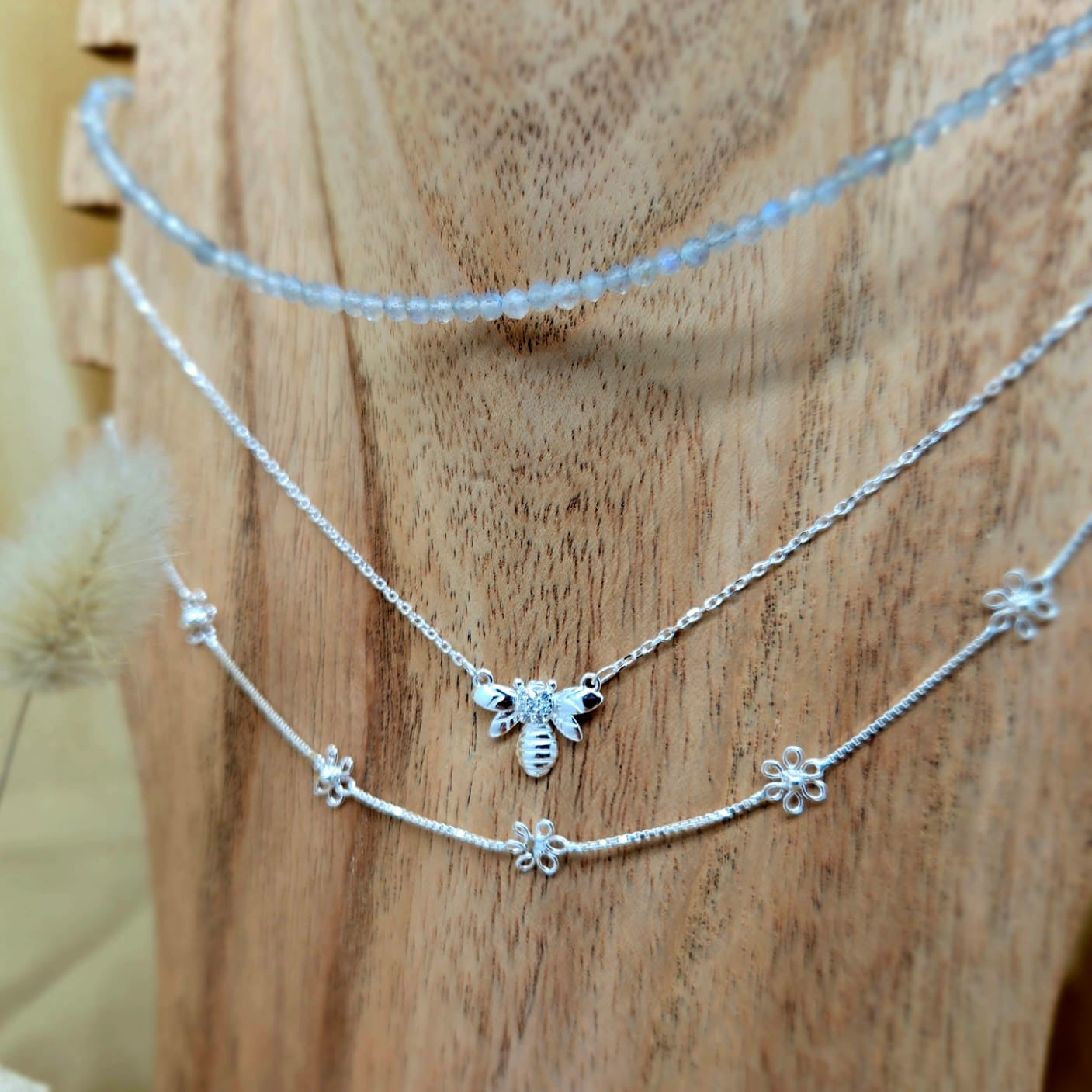 Two silver necklaces with bee and flower charms on a wooden surface