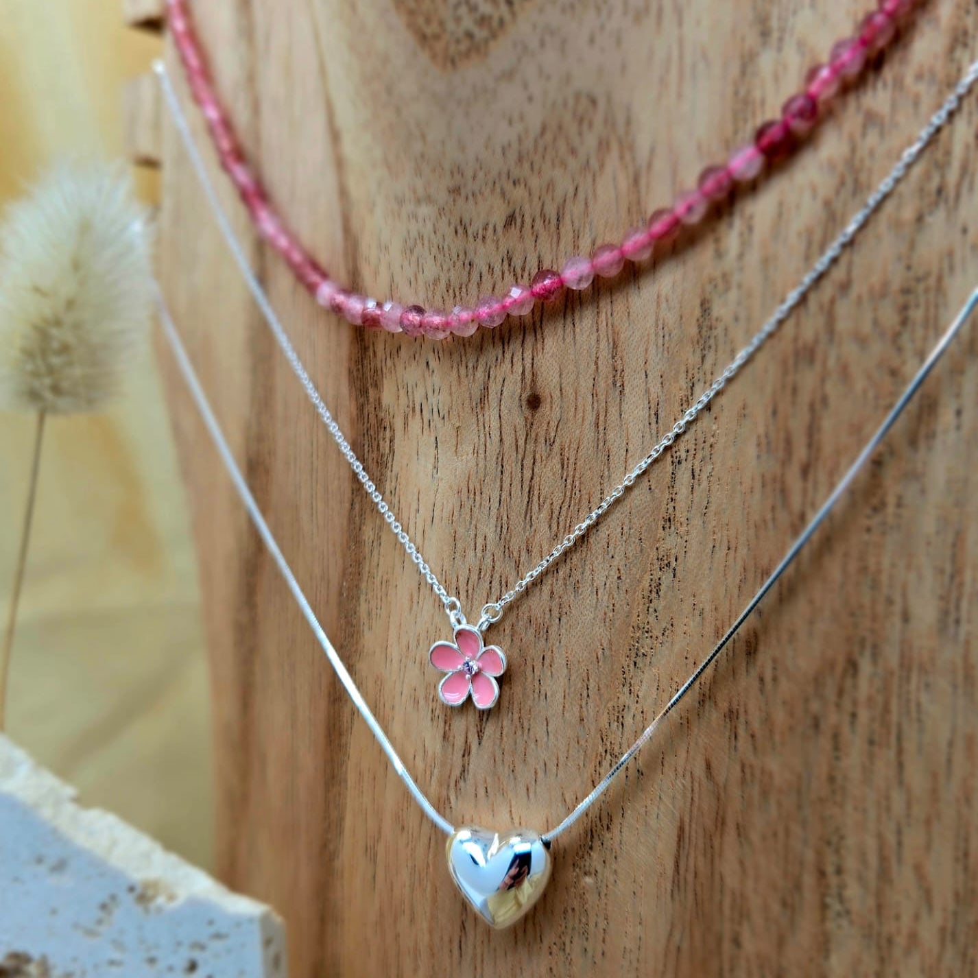Three necklaces with floral and heart pendants on a wooden surface.
