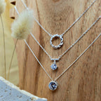 Three silver necklaces with circular pendants on a wooden surface