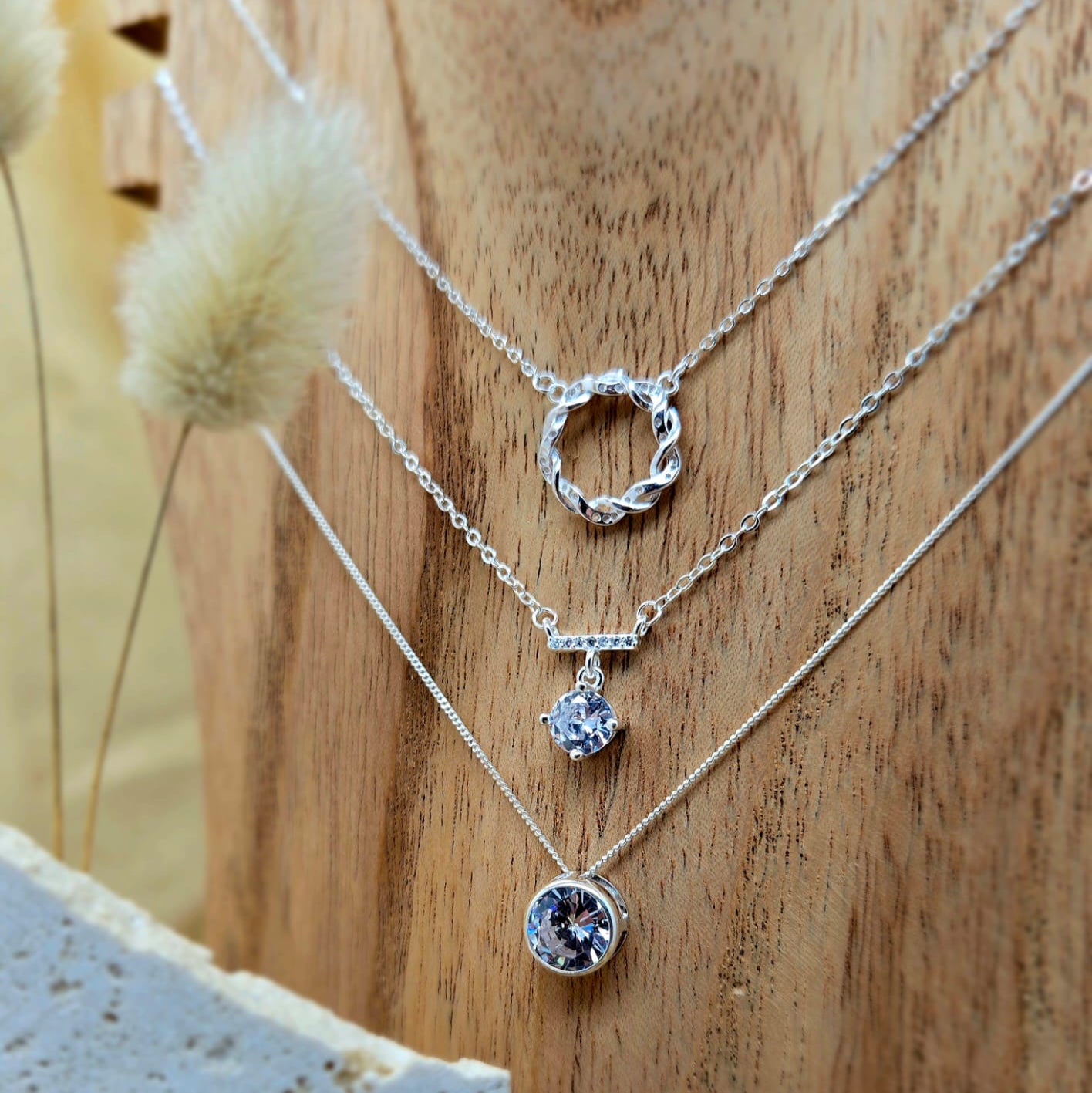 Three silver necklaces with circular pendants on a wooden surface