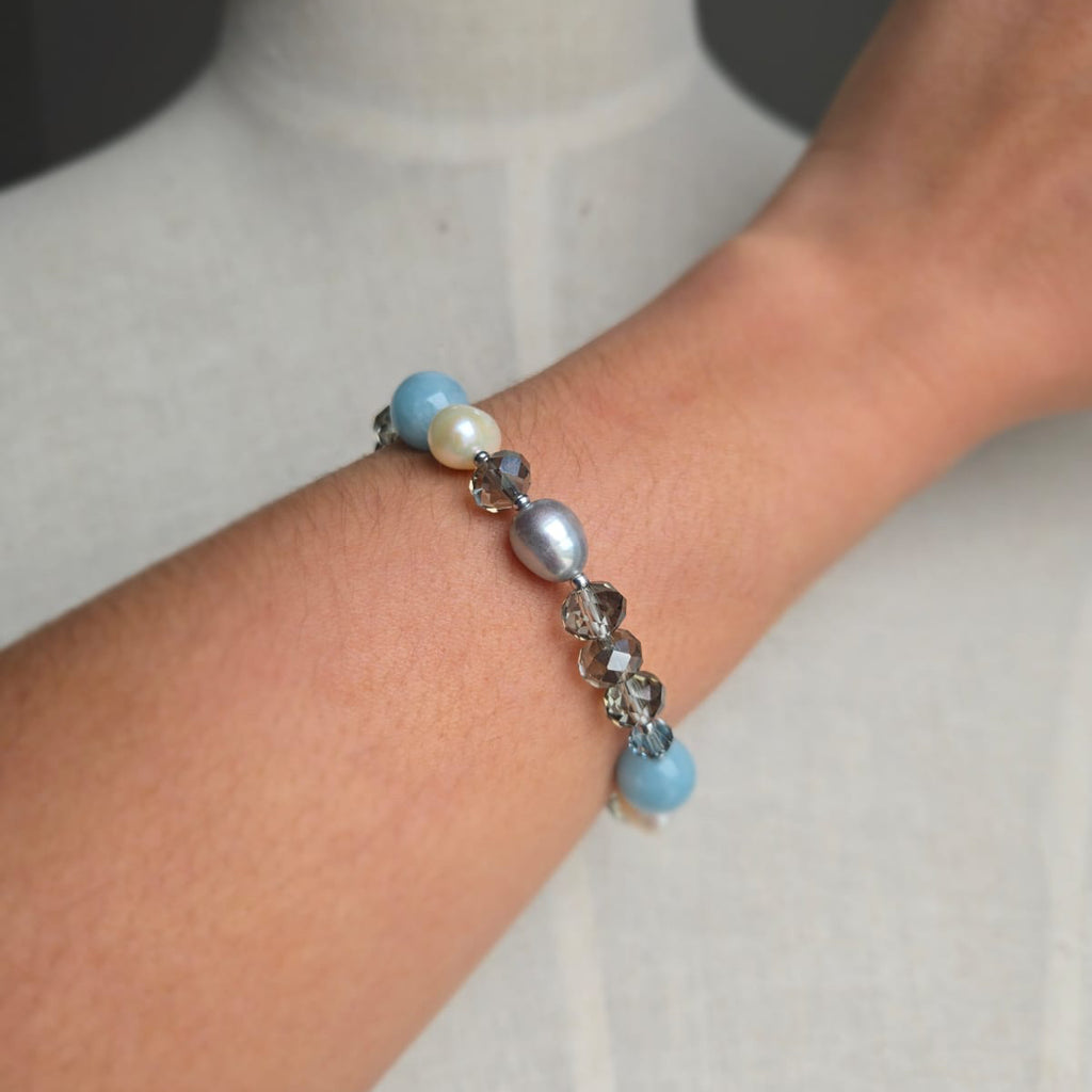 Bracelet with blue and pearl beads on a wrist against a neutral background