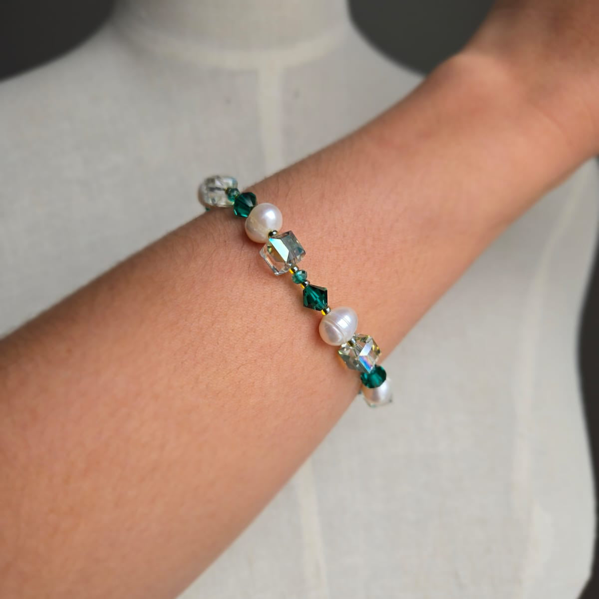 Beaded bracelet with green and clear beads on a wrist against a neutral background