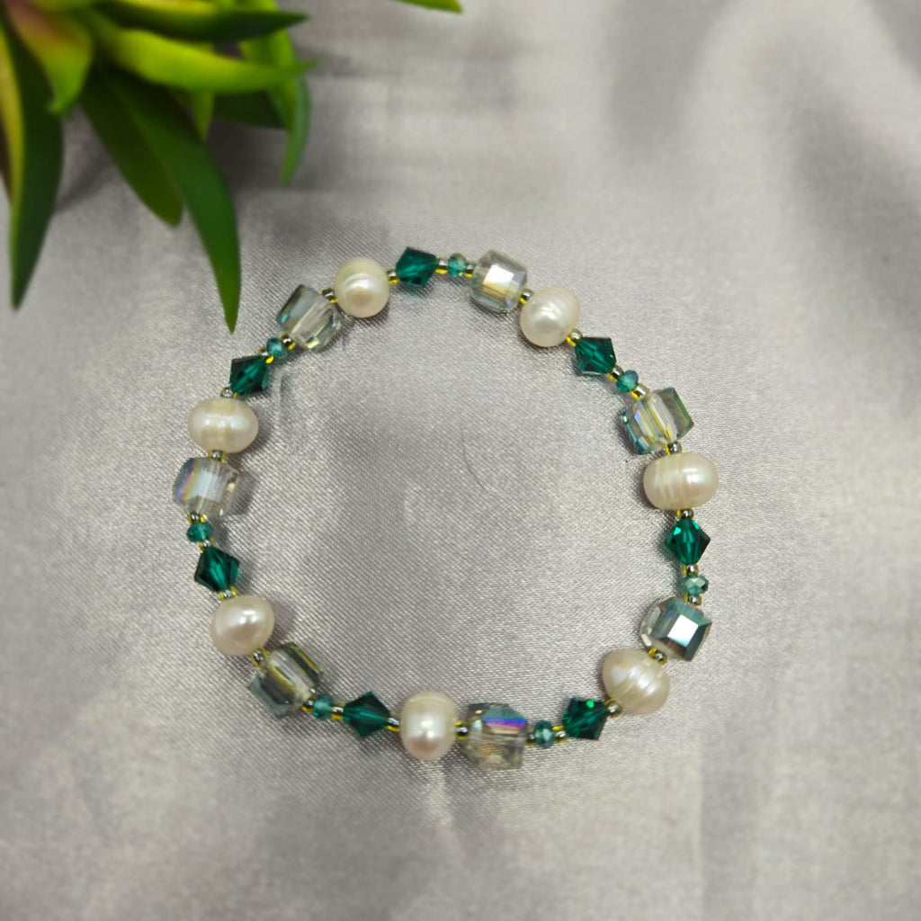 Beaded bracelet with pearls and green crystals on a gray fabric background