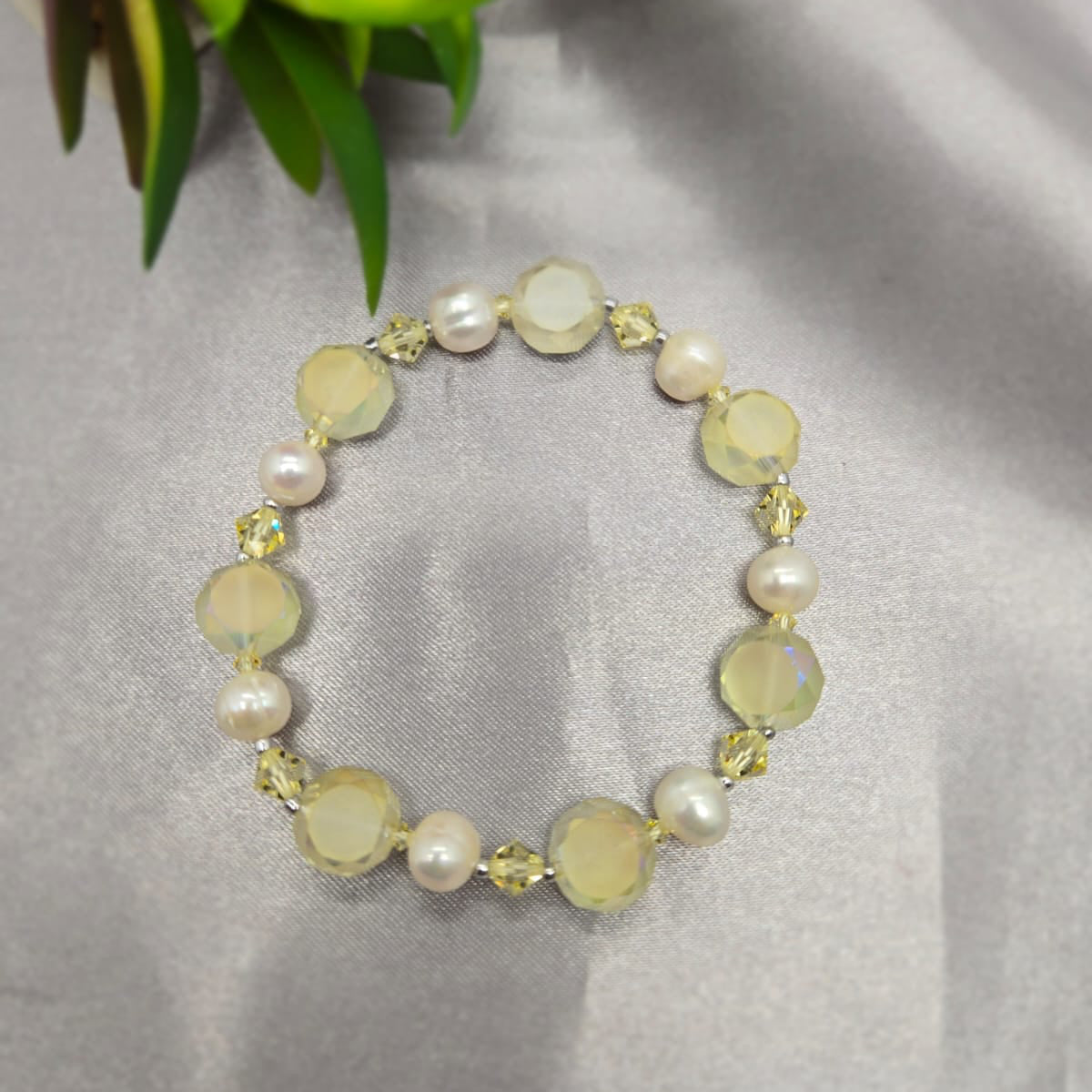 Bracelet with yellow and white beads on a gray surface with a plant in the corner