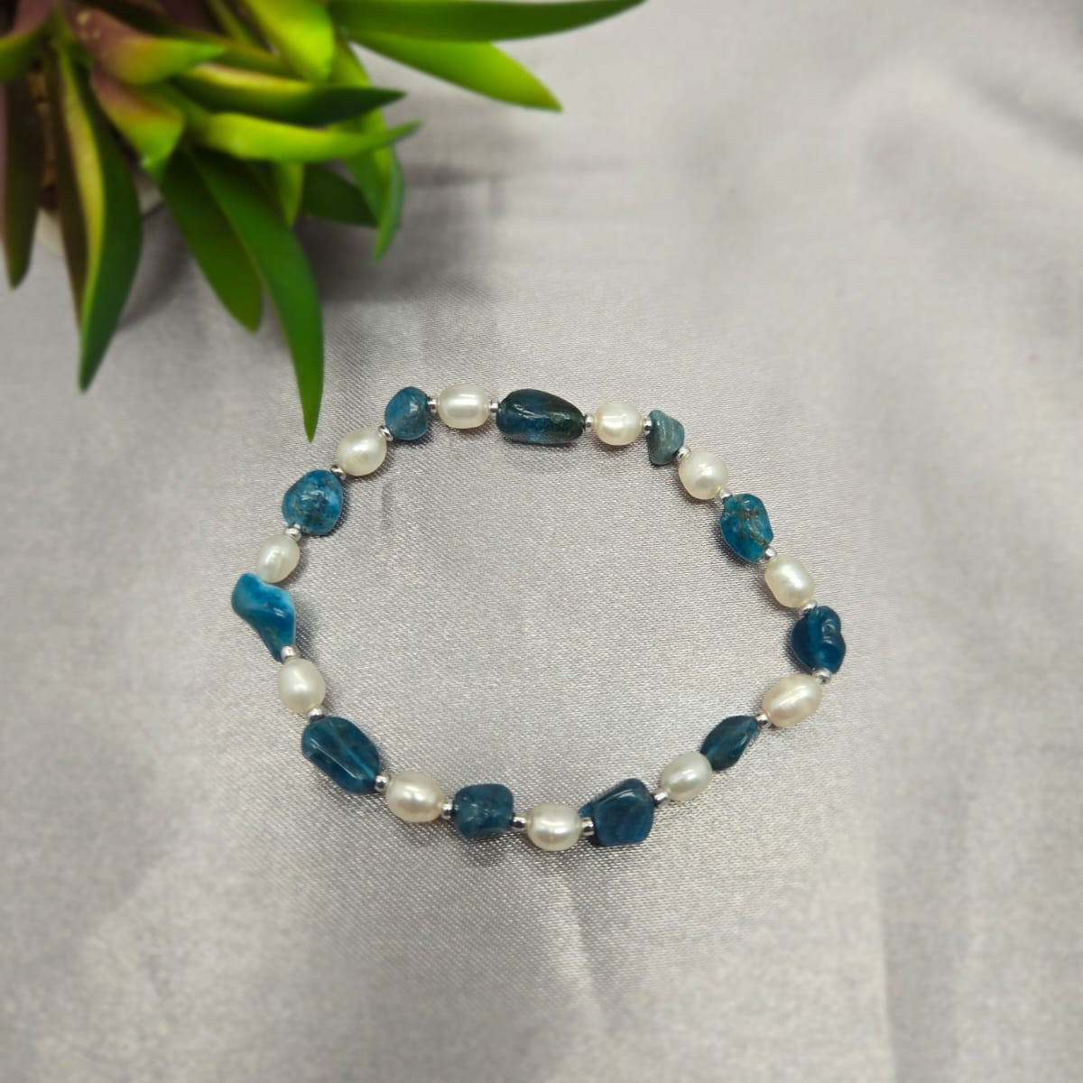 Bracelet with blue and white beads on a gray surface with a plant in the corner