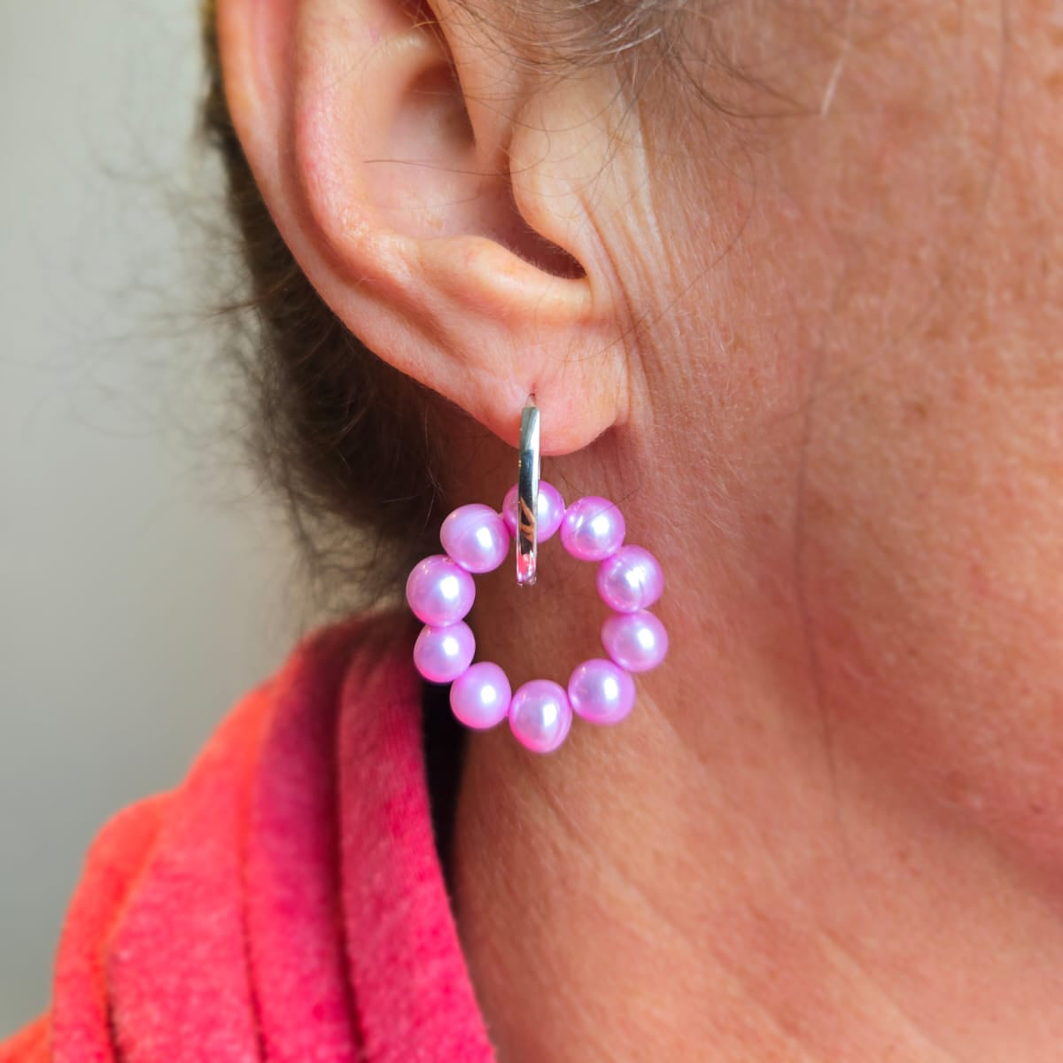 Close-up of an ear wearing a pink beaded hoop earring with a blurred background.