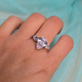 Hand wearing a ring with a pink gemstone against a light blue background