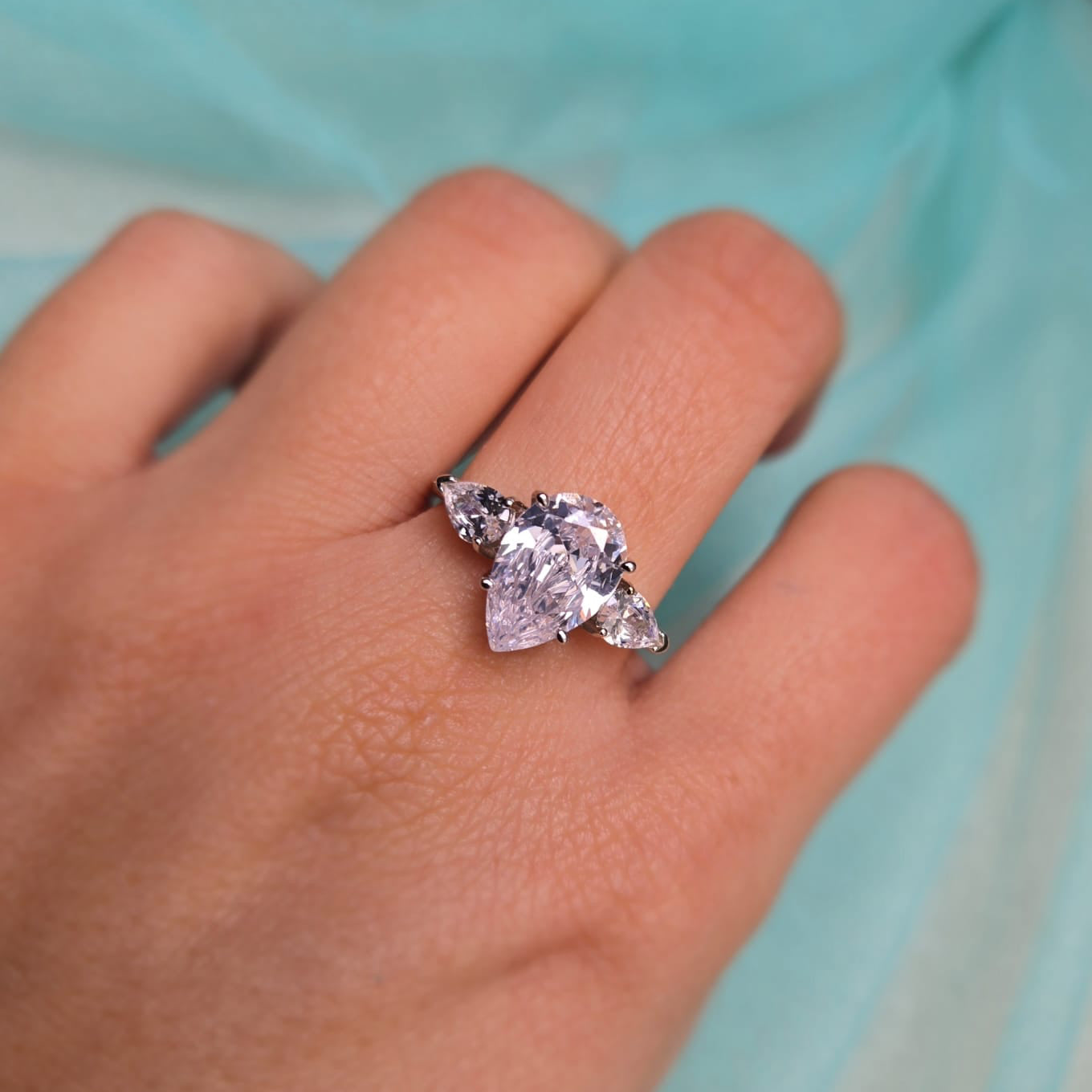 Hand wearing a ring with a pink gemstone against a light blue background