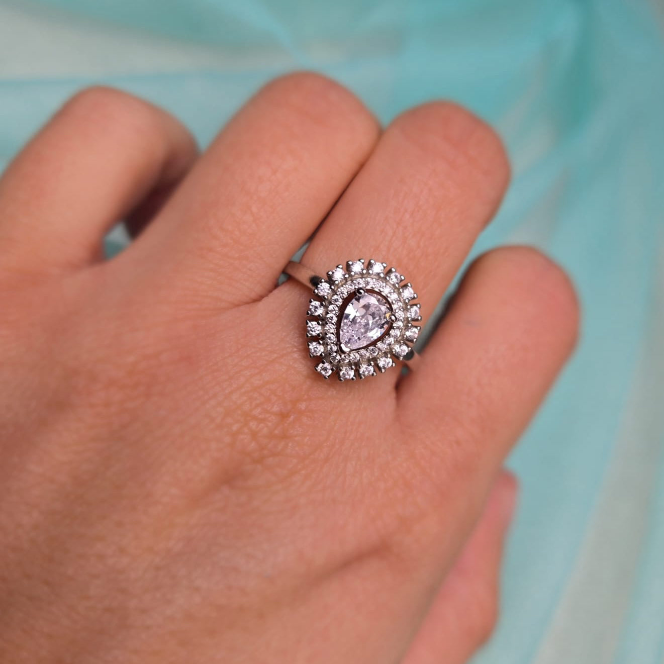 Close-up of a hand wearing a ring with a heart-shaped gemstone on a light blue background
