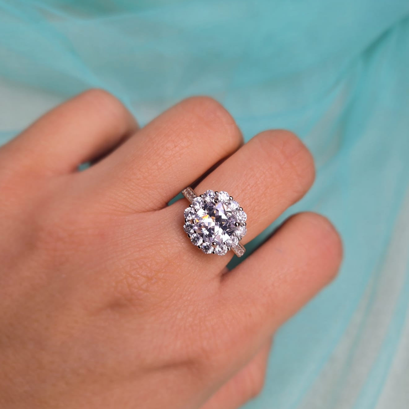 Close-up of a hand wearing a diamond ring with a light blue fabric background