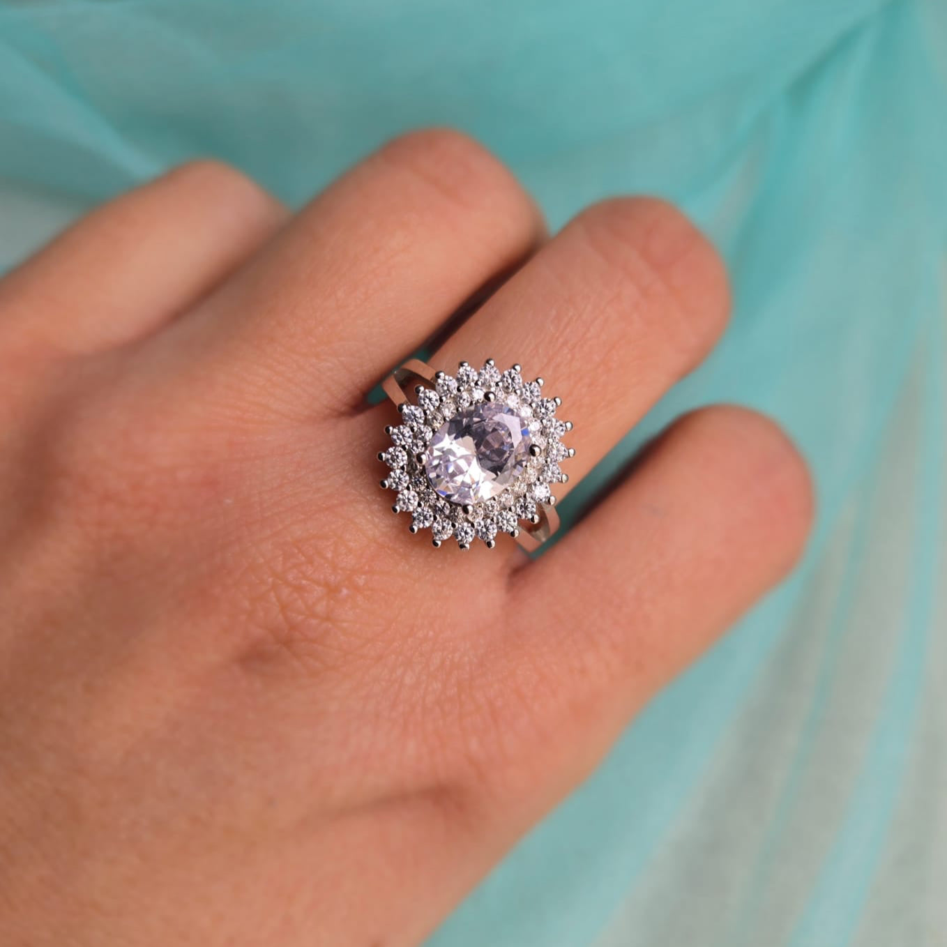 Silver ring with a large diamond on a hand against a light blue background