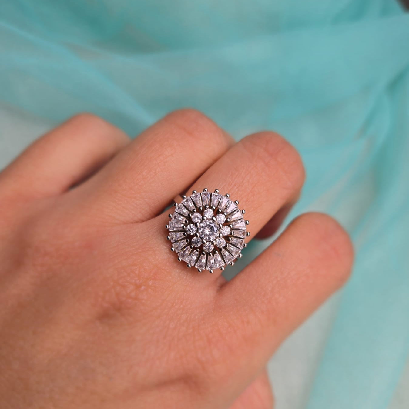 Silver ring with gemstones on a hand against a light blue fabric background