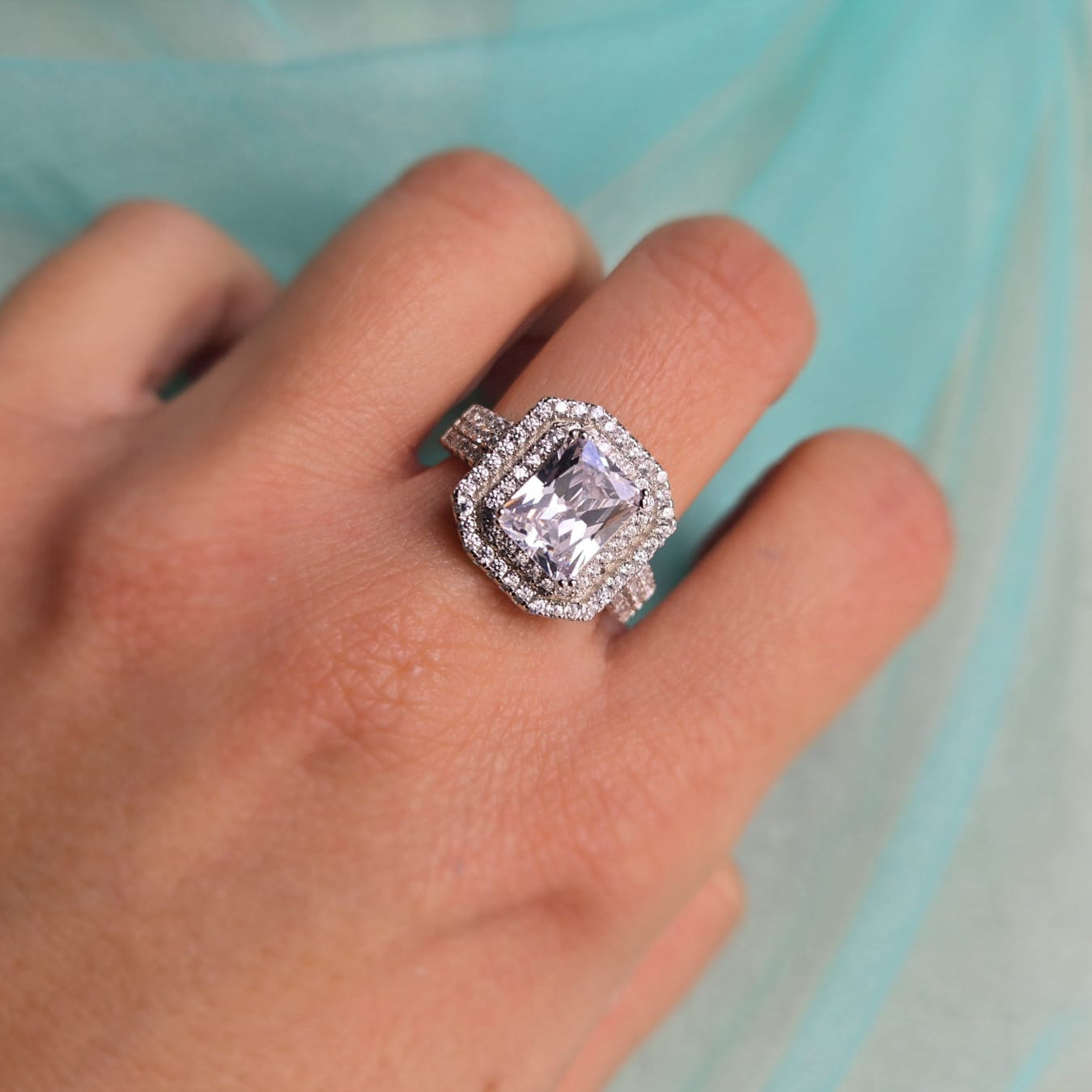 Silver ring with a large diamond on a hand against a light blue background