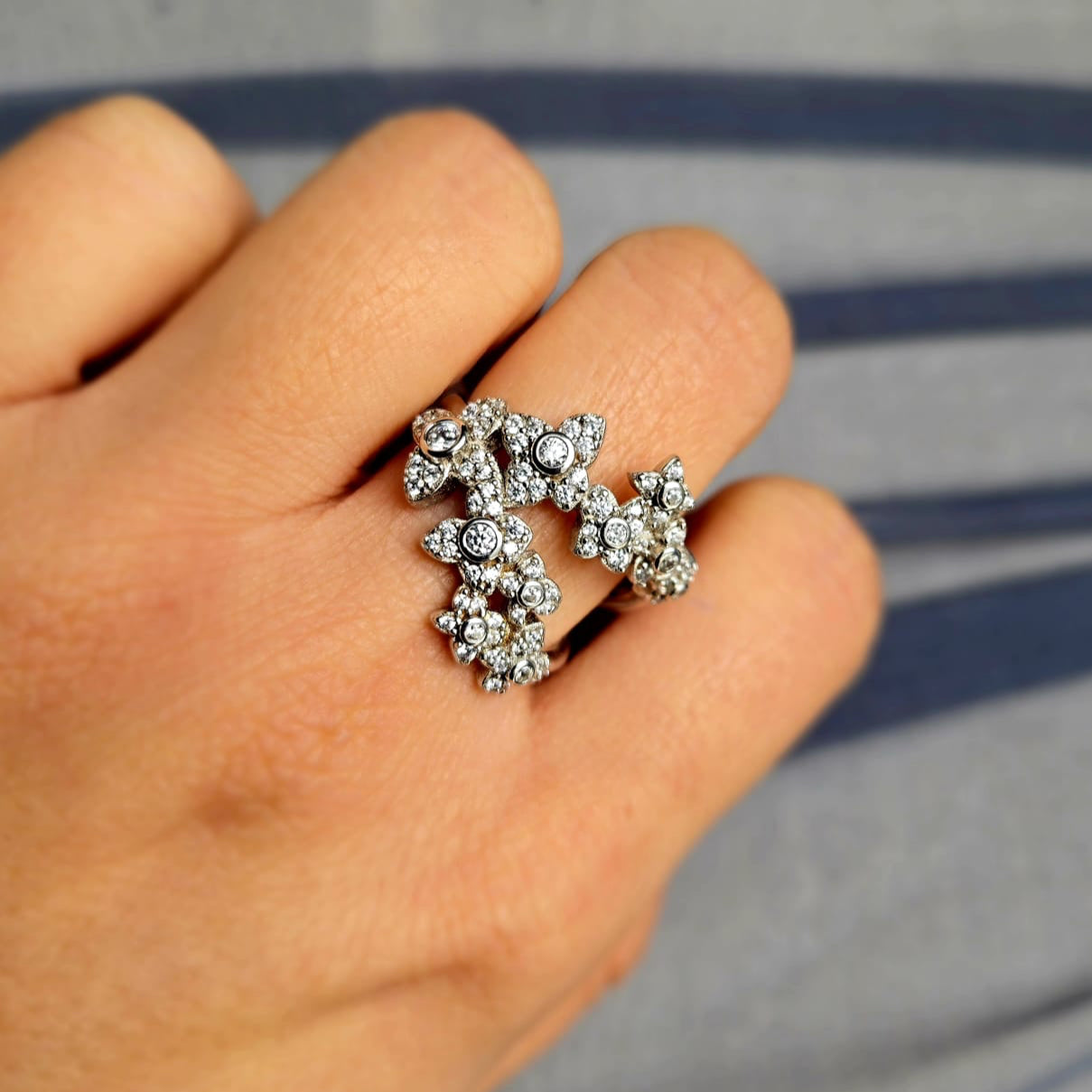 Silver ring with gemstones on a person's finger against a striped background